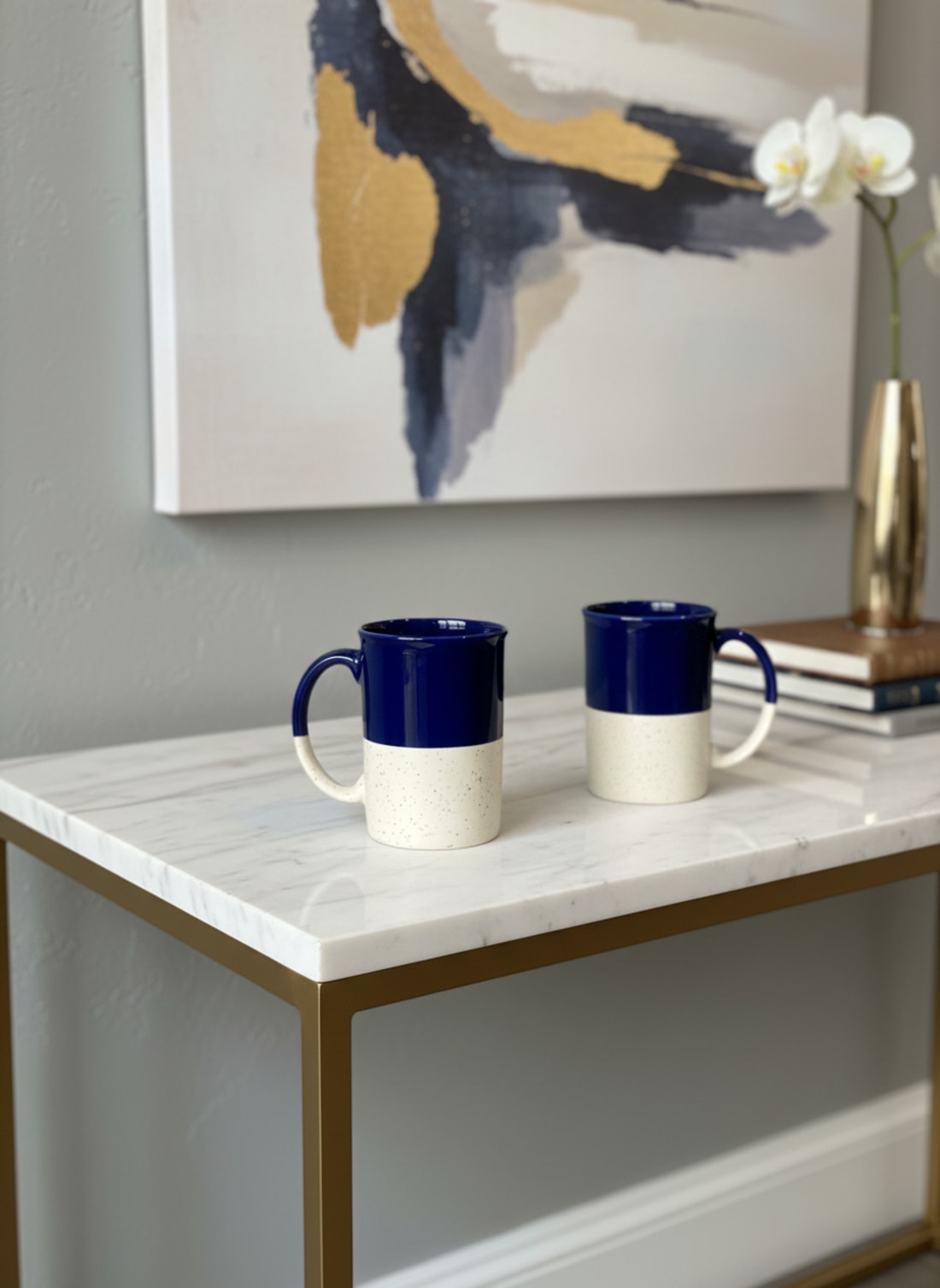 Handcrafted set of two ceramic coffee mugs with a blue and speckled cream dual-tone glaze on a marble console table.