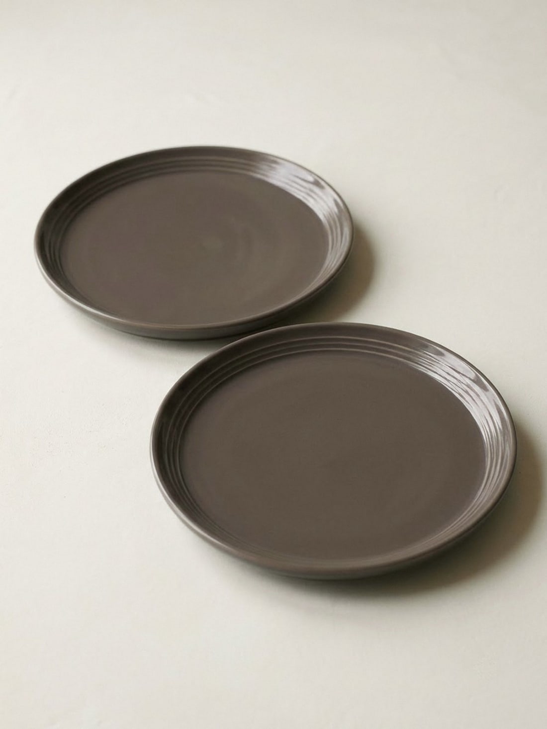 Set of 2 taupe-brown satin-glaze ceramic snack plates, 7.5 inch, with three raised rings on the rim, on an off-white plaster surface