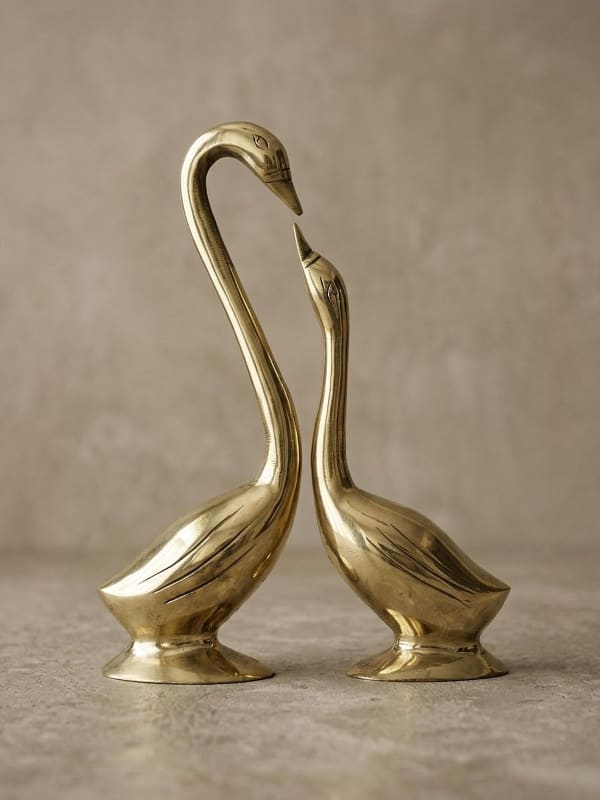 Pair of polished brass swans on oval pedestals facing each other, the taller swan's bowed neck and the smaller swan's raised beak forming a heart
