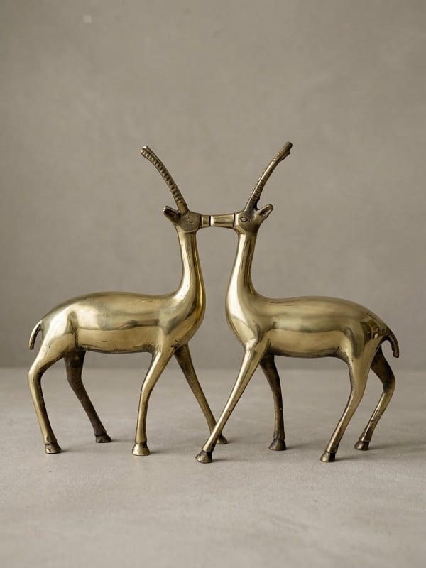 Pair of polished brass antelope figurines standing nose to nose, their square muzzles touching and long ridged horns rising in a V