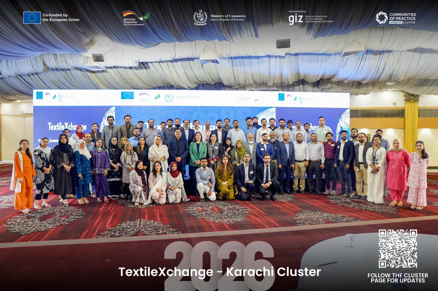 Large group photo of TextileXchange 2026 Karachi Cluster participants standing together in front of the conference stage with partner logos and event branding visible.