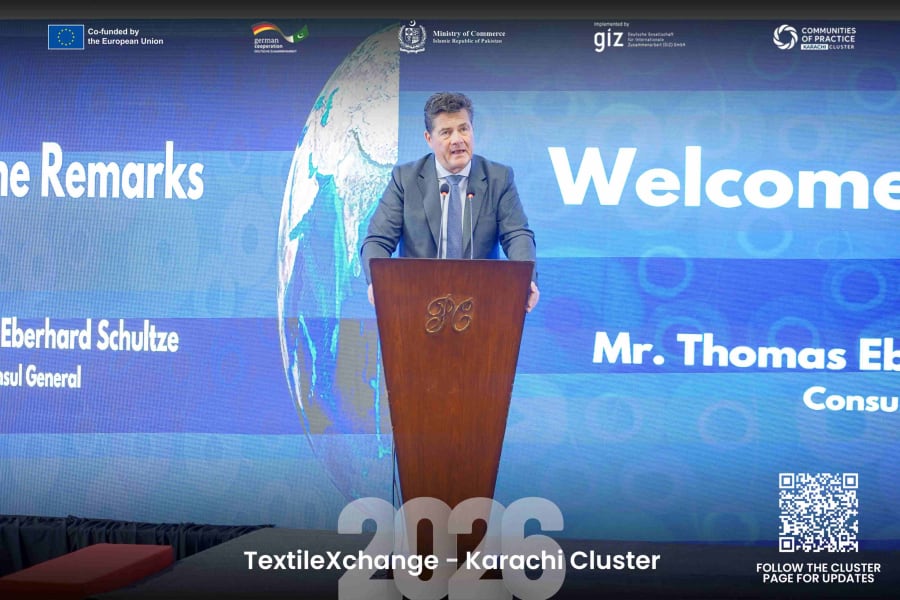 German Consul General Thomas Eberhard Schultze speaking at a podium during TextileXchange 2026, with the conference screen and partner logos in the background.