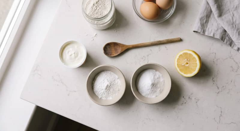 Bowls of baking powder and bicarbonate of soda beside yoghurt and lemon on a kitchen counter