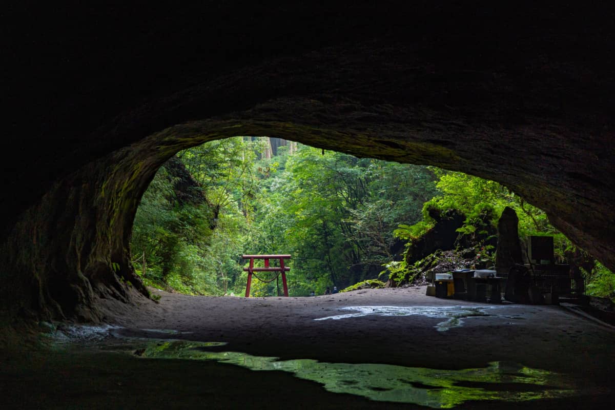 The dramatic cave entrance of Mizonokuchi Cave framed by greenery and traditional Shinto elements