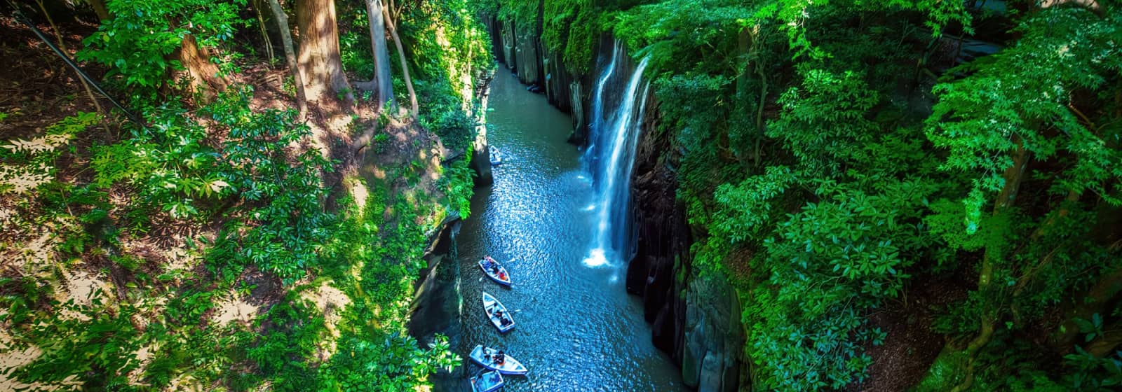 Looking down at river full of boats from a cliff with trees in Japan