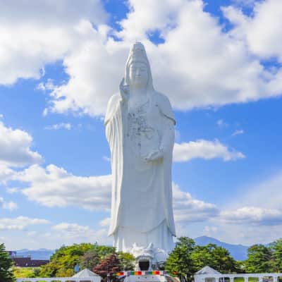 A massive white Kannon statue towers above Sendai City at Daikanmitsuji Temple, with visitors exploring the serene Buddhist interior filled with statues, spiral staircases, and panoramic viewpoints overlooking Miyagi Prefecture.