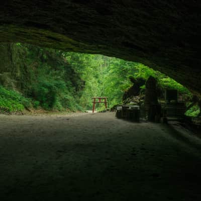Entrance of Mizonokuchi Cave featuring a red torii gate surrounded by lush forest in Kagoshima, Japan