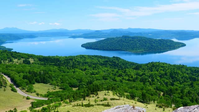 Expansive caldera lake featuring clear waters, volcanic terrain, and panoramic mountain views in eastern Hokkaido