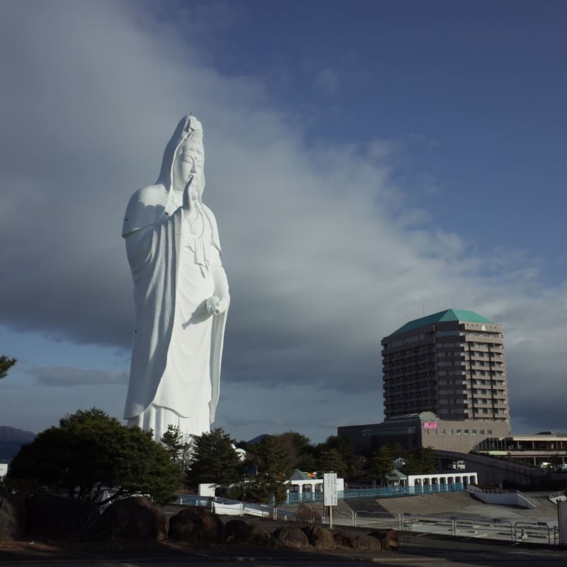 A massive white Kannon statue towers above Sendai City at Daikanmitsuji Temple, with visitors exploring the serene Buddhist interior filled with statues, spiral staircases, and panoramic viewpoints overlooking Miyagi Prefecture.