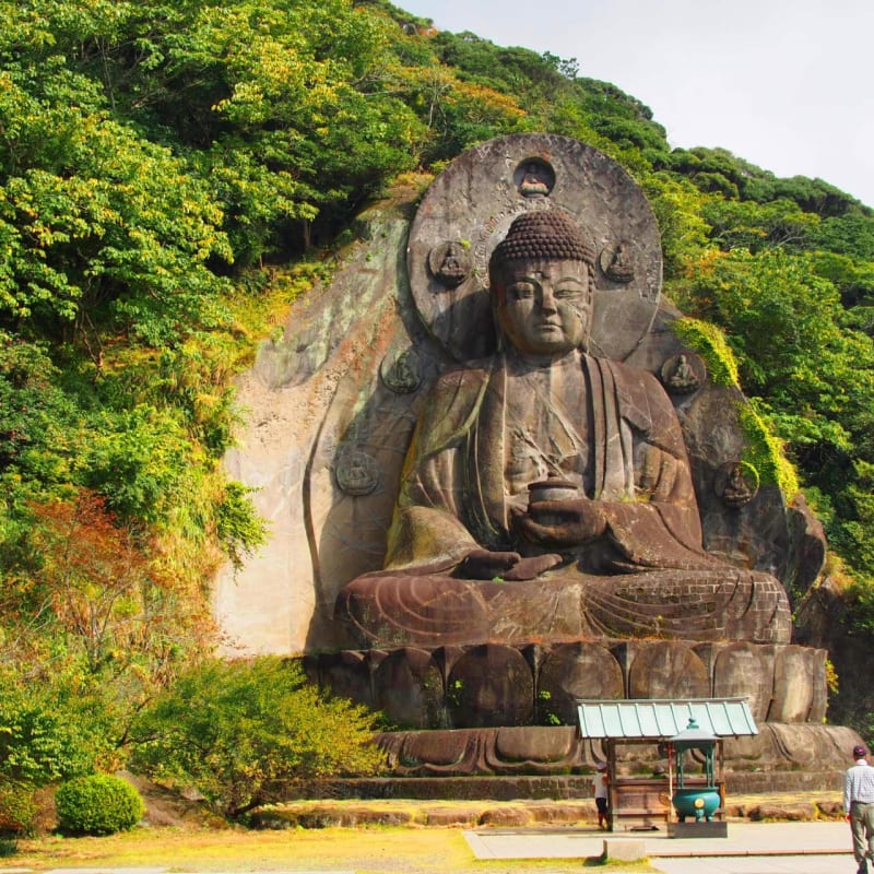 The towering Nihon-ji Daibutsu carved into the mountainside of Mount Nokogiri in Chiba, surrounded by forested temple grounds.
