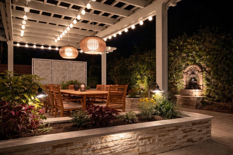 Pergola with string lights over a dining table and lit stone planter at night