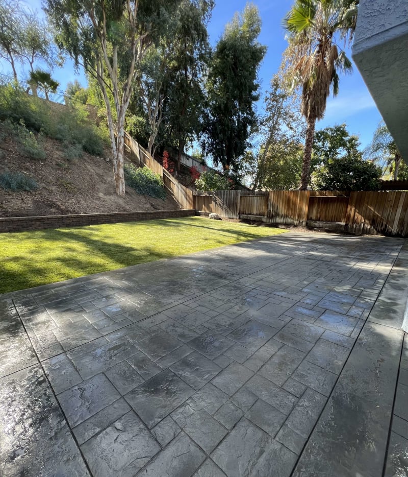 Gray stamped concrete patio beside a lawn and hillside