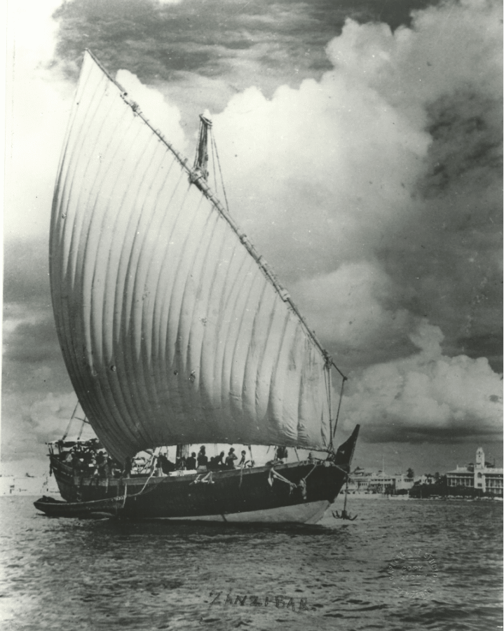 Black and white photograph of a boat on the sea with buildings in the near distance.