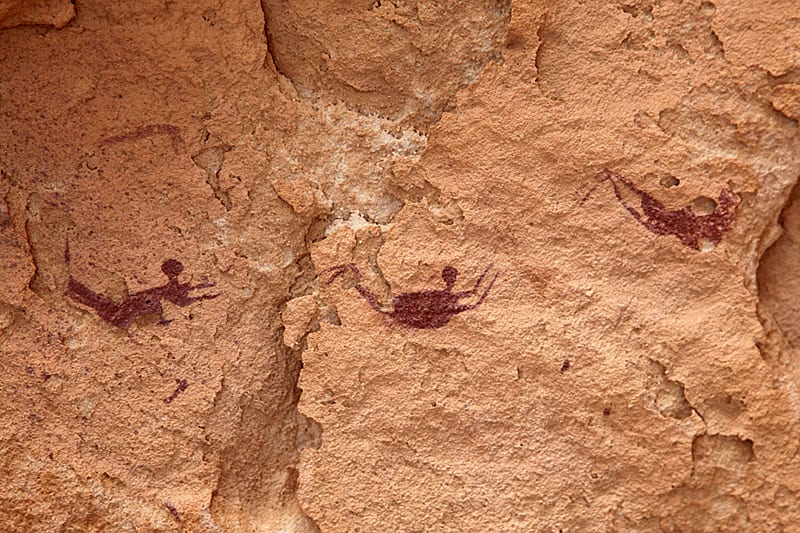 three human figures that appear to be swimming, painted in red-brown on on rock