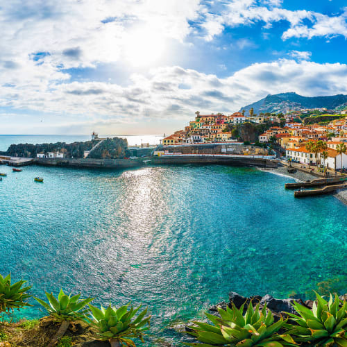 A picturesque coastal town nestled between mountains, with colorful buildings lining the harbor and crystal-clear turquoise waters in the foreground.
