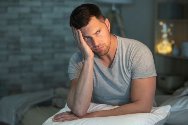 A sad man sitting on his bed and holding a pillow