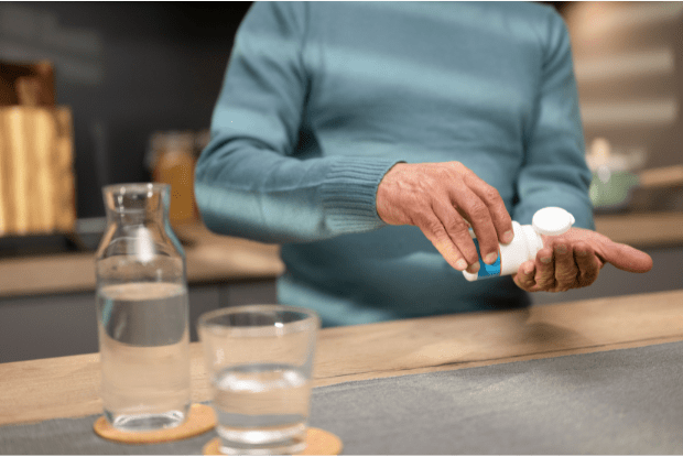 A man taking a pill with a glass of water on the table.