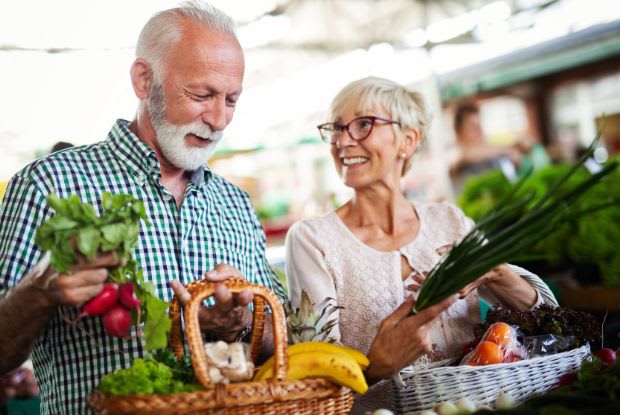 An elderly couple carrying baskets of fruits and vegetables