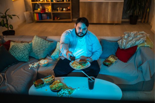 an overweight man eating in front of the television