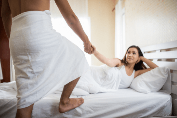 a woman pulling a man back into bed