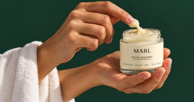 A hand, a towel over the arm, scoops balm from an open jar of MARL natural deodorant