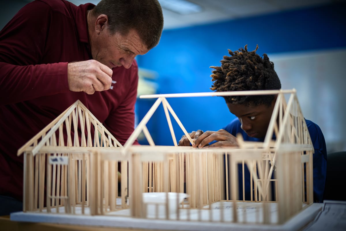 A student and teacher building a wooden truss model of a house