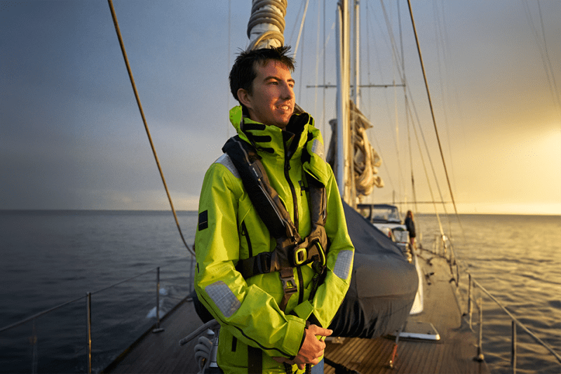 A student in foul-weather gear on deck at sunset during a sailing expedition