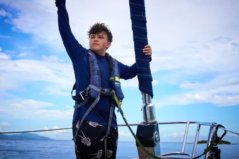A student in a harness reaching up the mast at the bow