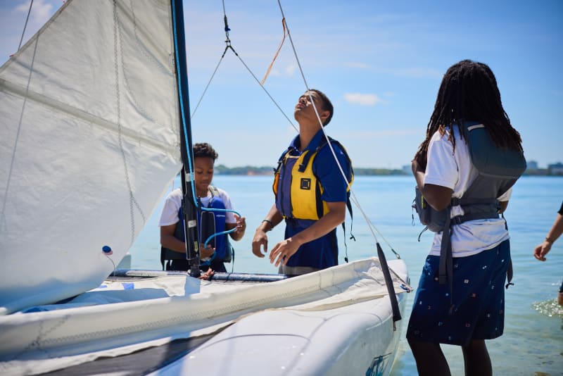 Students rigging a catamaran at the water's edge