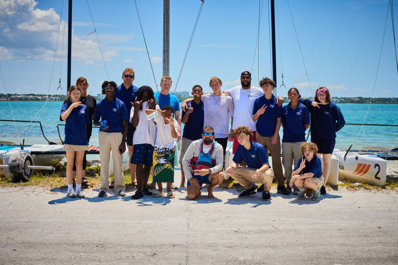 Students and staff together on the dock beside the sailboats