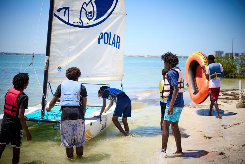 Students launching a small catamaran from the beach