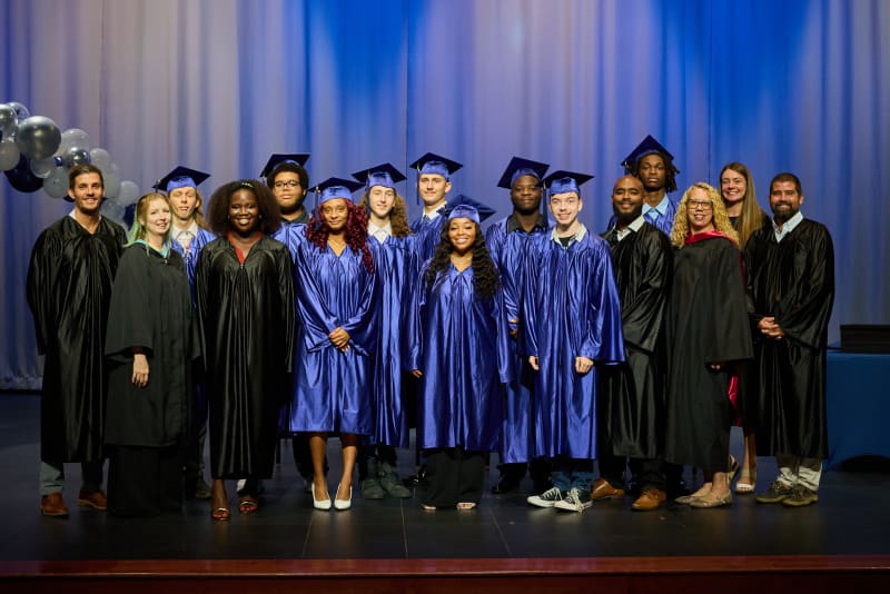 The graduating class in caps and gowns on stage with their teachers