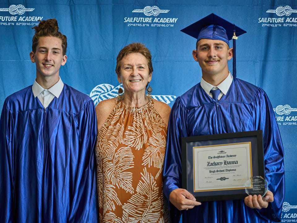 Graduates celebrate their academic milestone alongside a staff member at the Class of 2026 graduation ceremony.