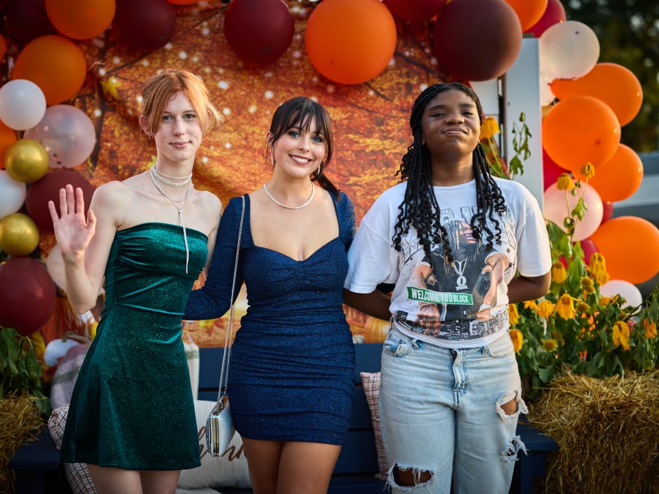 Three students pose cheerfully in front of a festive balloon arch at the homecoming event.