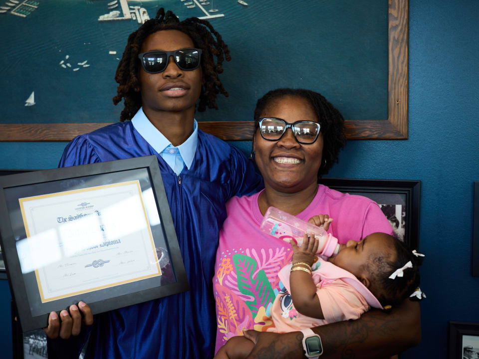 A proud graduate poses with family during a graduation celebration, highlighting a milestone achievement for the SailFuture community.