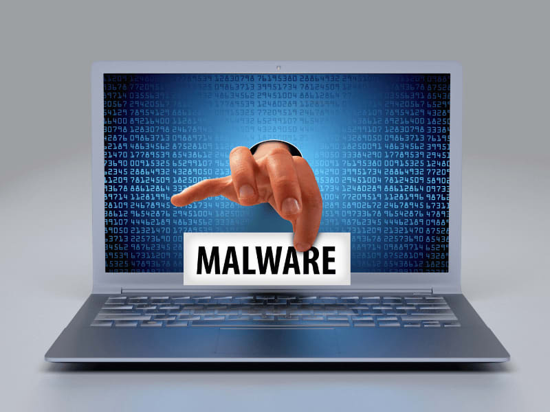 A digital hand labeled "Malware" reaching through a laptop screen, symbolizing malware threats.