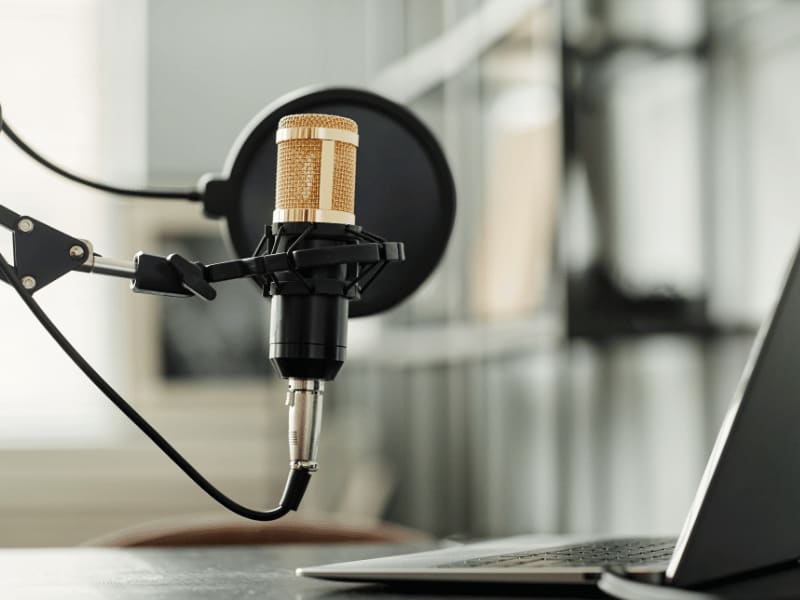 Professional studio microphone with a pop filter connected to a laptop, used for voice recording or streaming.
