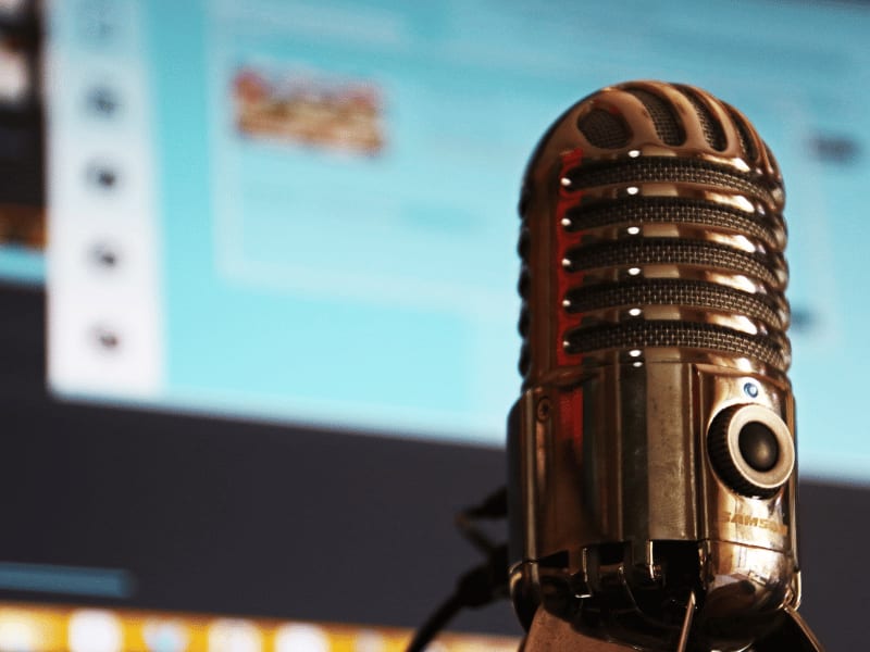 Close-up of a retro microphone in front of a computer screen, symbolizing audio recording or podcast setup.