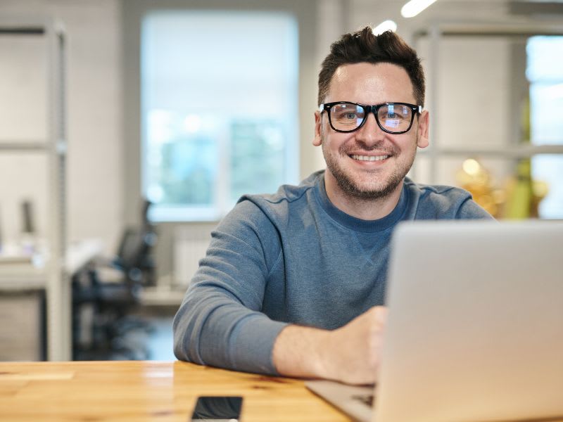 Smiling man working on a laptop in an office, representing the importance of data recovery services.