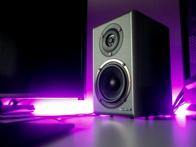 Two black desktop speakers on a reflective surface under soft blue lighting