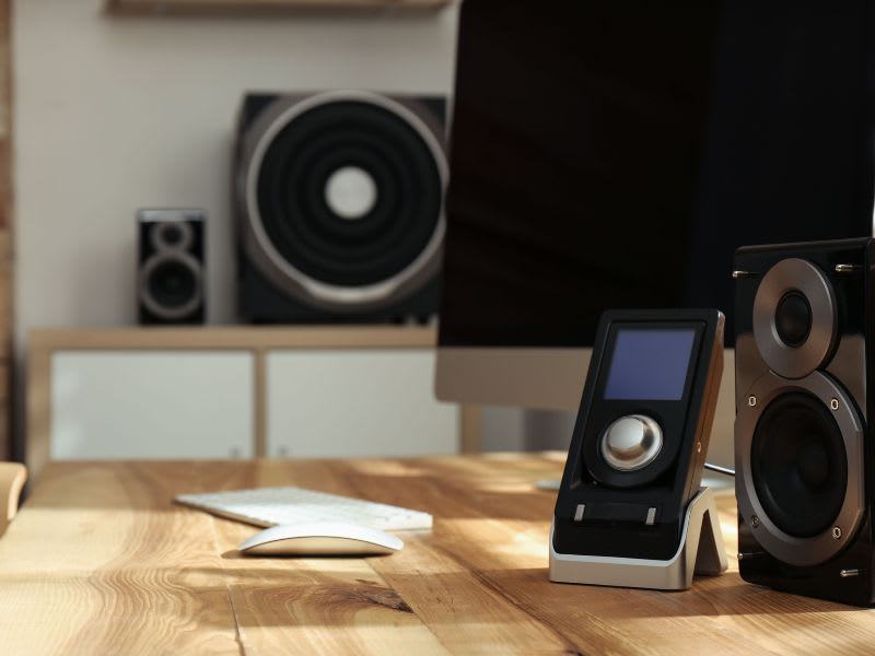 Computer speakers on a wooden desk with an iMac and audio control interface