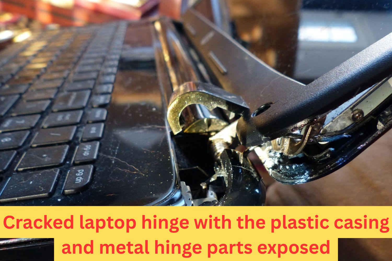Close-up of a broken laptop hinge with visible damage to the casing and exposed charging port area, showing structural failure near the screen.