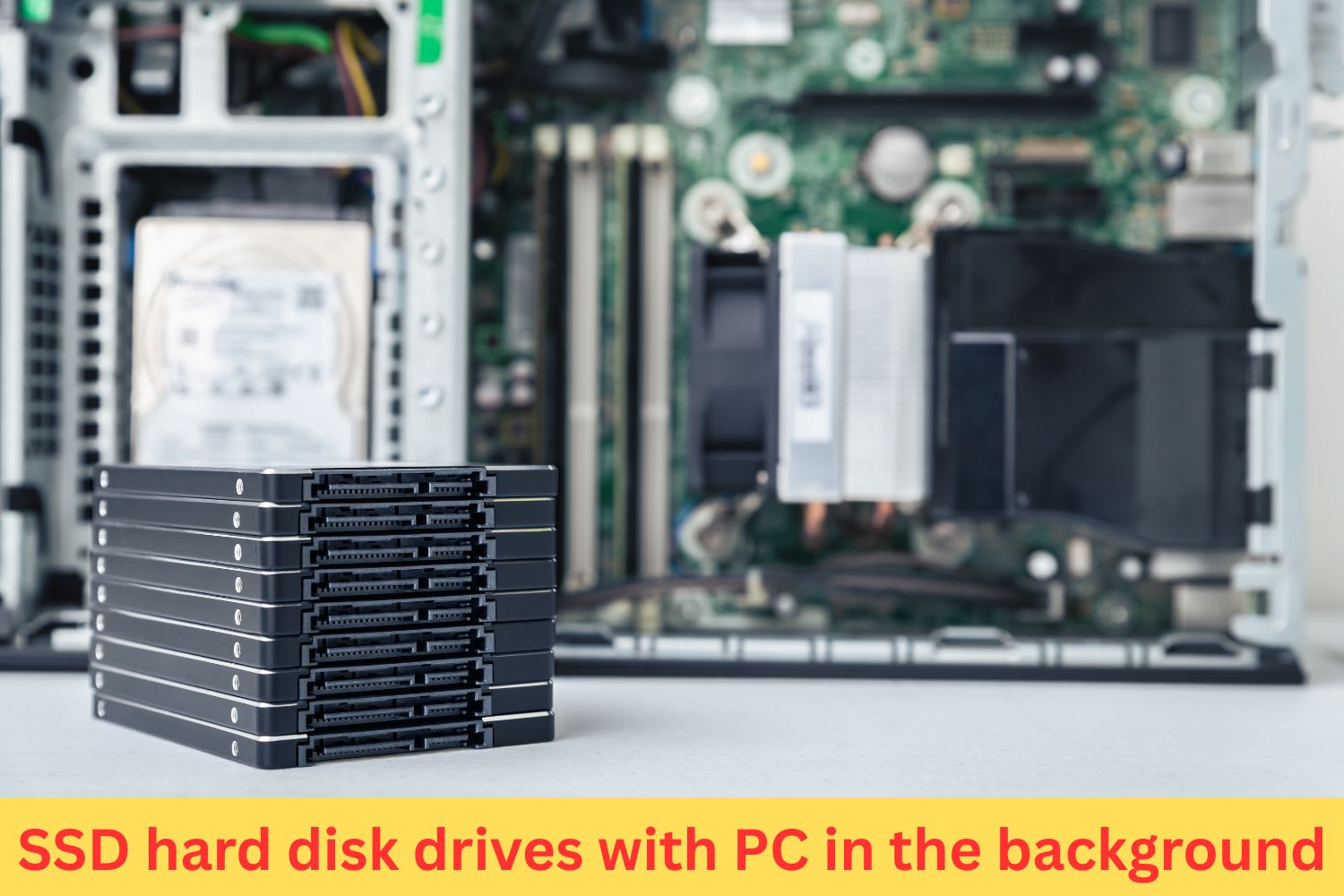 Stack of solid-state drives (SSD) placed in front of an open desktop computer showing motherboard components in the background