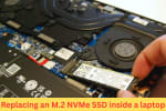 Close-up of a person replacing an M.2 NVMe SSD inside a laptop, showing internal components like the battery, fan, and motherboard.