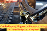 Close-up of a broken laptop hinge with visible damage to the casing and exposed charging port area, showing structural failure near the screen.