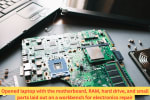 Opened laptop with motherboard, RAM, and parts laid out on a table during component-level electronics repair.