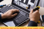 Technician opening up a laptop using screwdrivers to access the internal power components for power supply troubleshooting or repair.