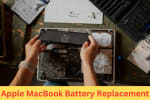 Technician replacing an Apple MacBook battery with the laptop opened on a desk, surrounded by repair tools and guidebooks