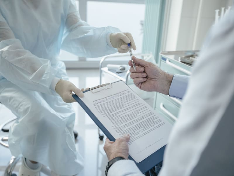 Doctor handing insurance claim paperwork and a clipboard to a patient for signature before BPH treatment