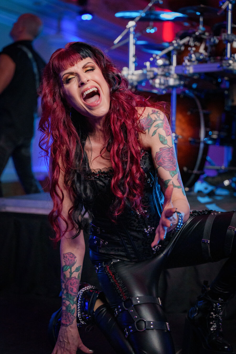 Gros plan de la chanteuse aux cheveux rouges et noirs en plein cri, en corset et pantalon de cuir, sous une lumière bleue